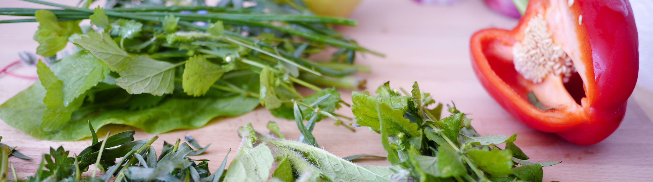 Close-up of fresh green herbs and a halved red bell pepper on a wooden cutting board