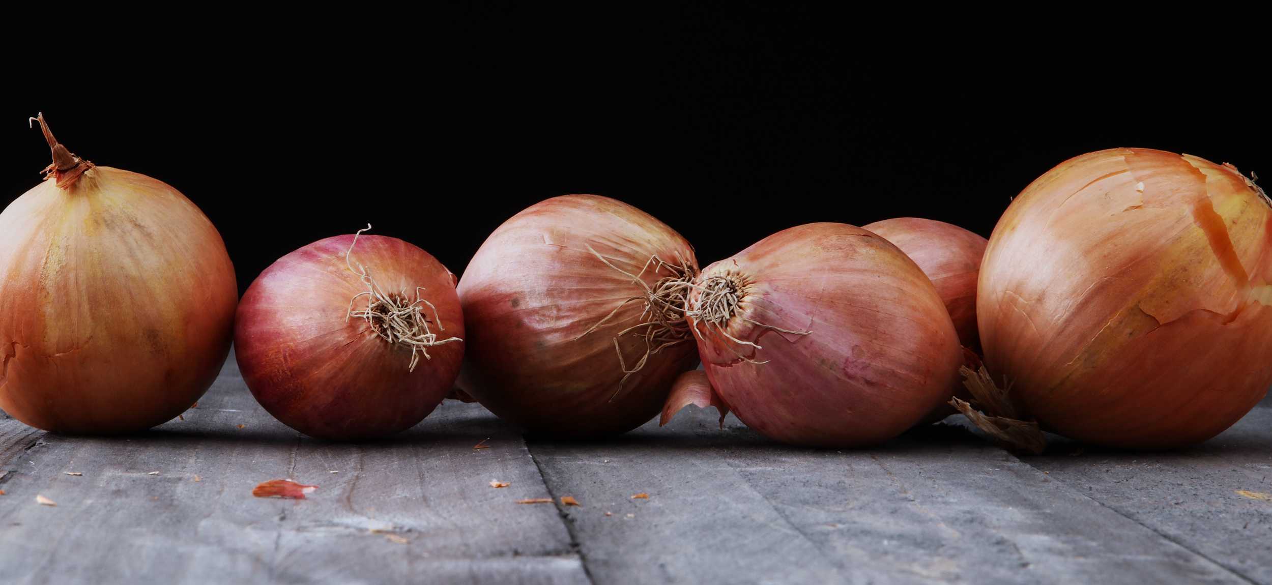 Row of onions with reddish and golden skins on a dark wooden surface, black background